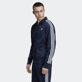 Adidas Firebird Track Jacket Men's in collegiate navy, front view showing full zip, stand-up collar, white 3-Stripes on sleeves, and Trefoil logo worn my model